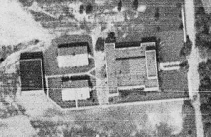 Black and white aerial photograph of Herndon High School taken in 1937. The building is shaped like the letter ‘I’. The two vocational classroom buildings and gymnasium are visible at the rear of the building. There are cement walkways connecting the buildings to one another. 