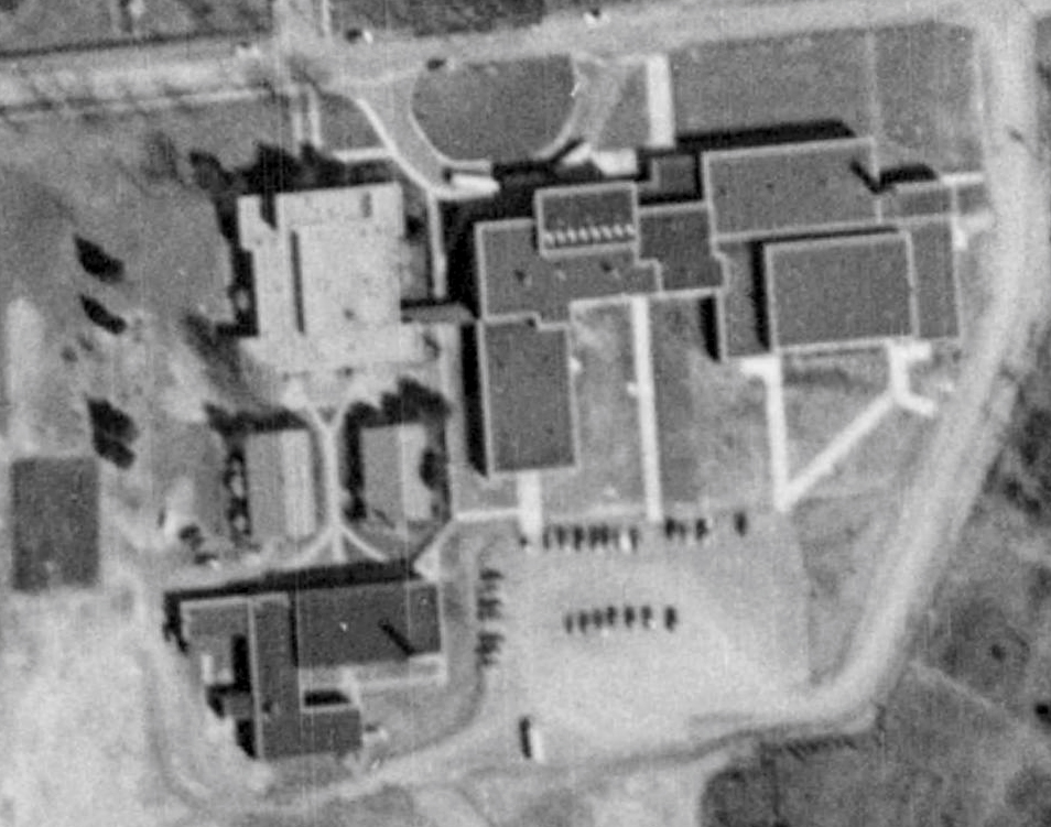 Black and white aerial photograph of Herndon High School taken in 1953. The new building is visible to the right of the 1927 school. It is ‘L’ shaped and has six main sections. An ‘L’ shaped addition has been added to the original gymnasium. A covered walkway connects the two schools together.